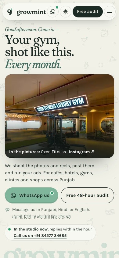 The studio’s home page on a phone: ‘Your gym, shot like this. Every month.’, the gym floor at Oxen Fitness under its lit sign, WhatsApp us and the free audit, the line on languages, and ‘In the studio now’.