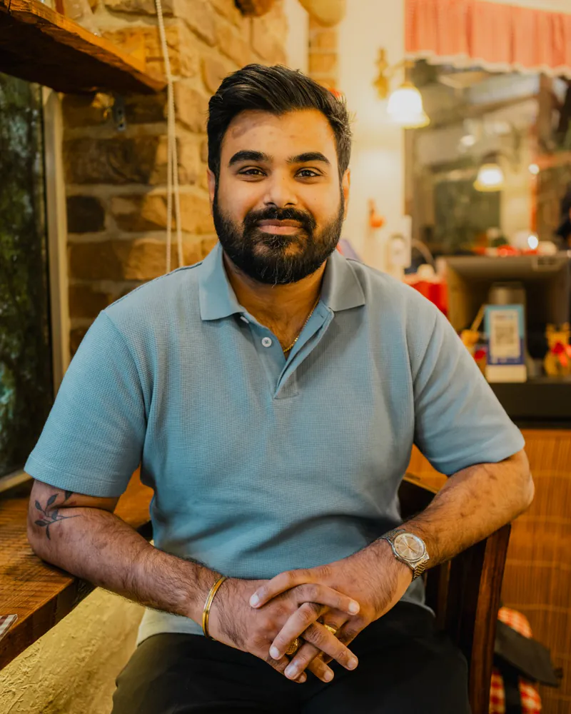 Aditya Vashistha, in a blue polo shirt, sitting in a café and smiling at the camera.